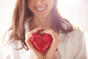 Frau hält lächelnd ein Herz als Zeichen für einen normalen Cholesterinspiegel