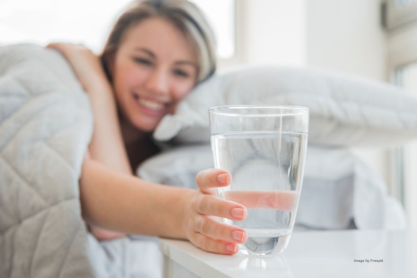 Frau mit Erkältung stellt ein Glas Wasser auf den Nachtisch