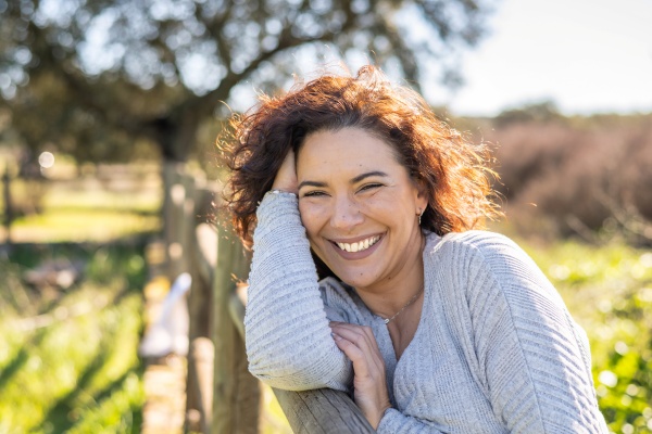An einem Zaun lehnende Frau lächelt voll Lebensfreude durch die Wirkung von Cordyceps