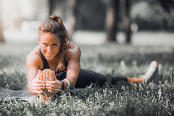 Sportliche, im Gras sitzende Frau mit höherem Bedarf an Magnesium durch Sport