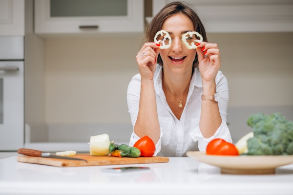 Frau hält Paprikascheiben vor ihre Augen als Ernährung gegen Falten