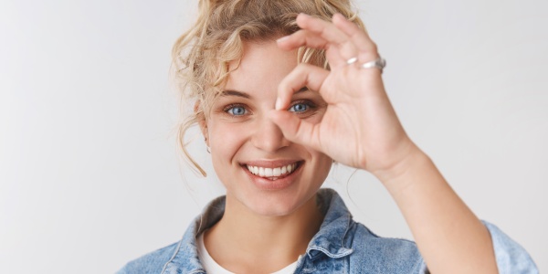 Eine junge Frau zeigt fröhlich mit dem Kreis, den Daumen und Zeigefinger formen, dass Ihre Augen gesund sind.