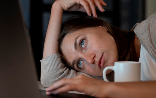 Frau lümmelt müde vor dem Laptop wegen Problemen mit der Leber