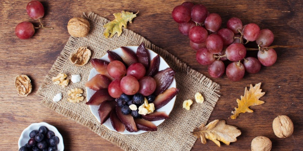Direkte Quellen von Resveratrol, Weintrauben und Nüsse, sind dekorativ auf einem herbstlich gedeckten Tisch angeordnet.