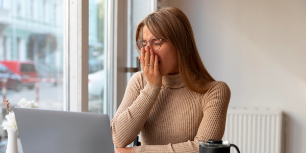 Frau sitzt am Laptop und ist ständig müde.