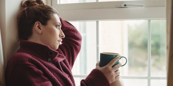 Frau sitzt kaffeetrinkend am Fenster und kämpft gegen Angst