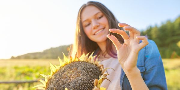Frau tankt in der Sonne Vitamin D und hält Sonnenblumenkern mit Magnesium