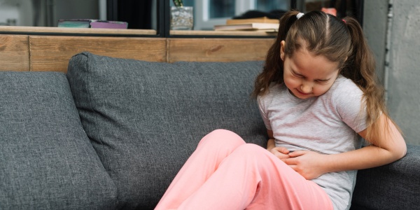 Kind am Sofa hält sich wegen Verstopfung gequält den Bauch 