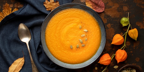 Süsskartoffel-Apfel-Suppe mit Kürbis und Kürbiskernen angerichtet auf einem herbstlich dekorierten Tisch.