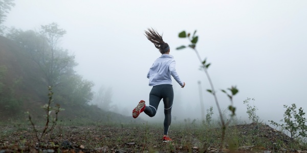 Sportlerin bei ihrem Lauftraining durch eine nebelige Herbstlandschaft.