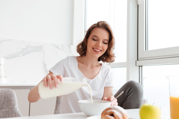 Frau leert Milch als calciumreiches Lebensmittel in eine Müslischüssel 