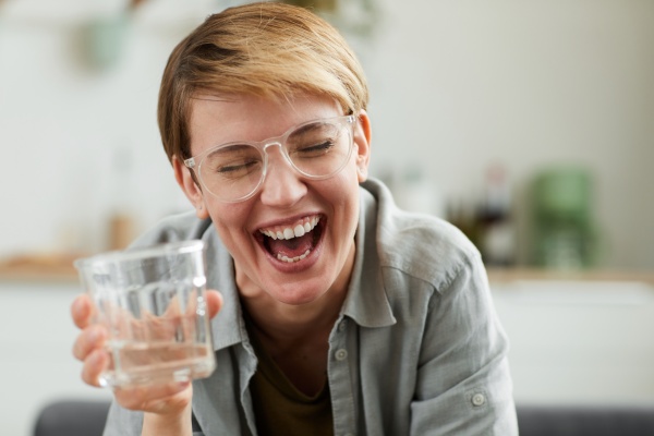 Frau mit einem Glas Wasser lacht und zeigt ihr gesundes Zahnfleisch