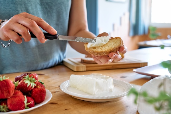 Frau streicht mageren Käse zur Ernährung für die Herzgesundheit auf Brot
