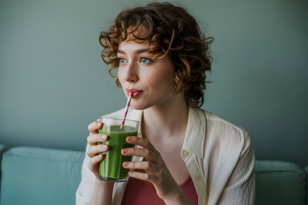 Frau trinkt Chlorella in einem grünen Smoothie