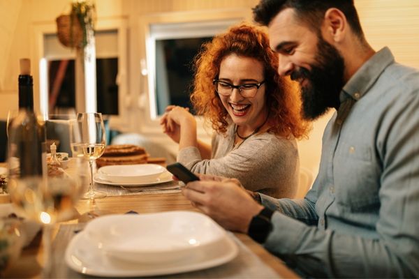 Mann und Frau beim Abendessen erkundigen sich am Handy, warum man Zink abends einnehmen soll