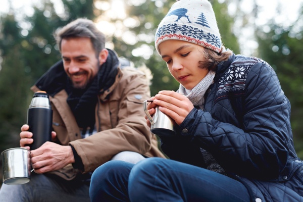 Mann und Mädchen mit heißem Getränk beim Wandern im Winter